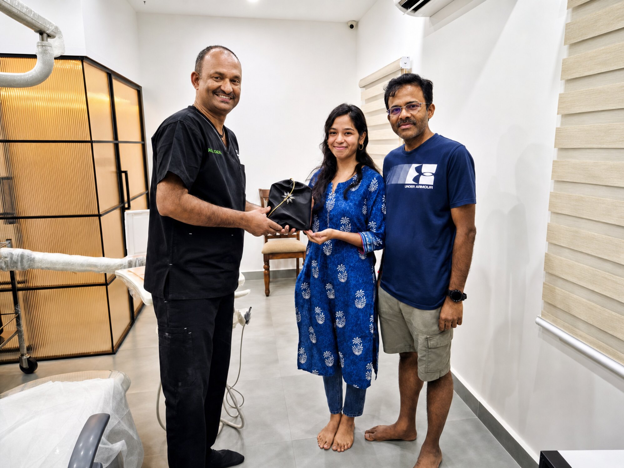 Prof. Dr S. Srinivas handing a patient her aligner case in a treatment room at Align Dental Care, her companion beside her, all three smiling.