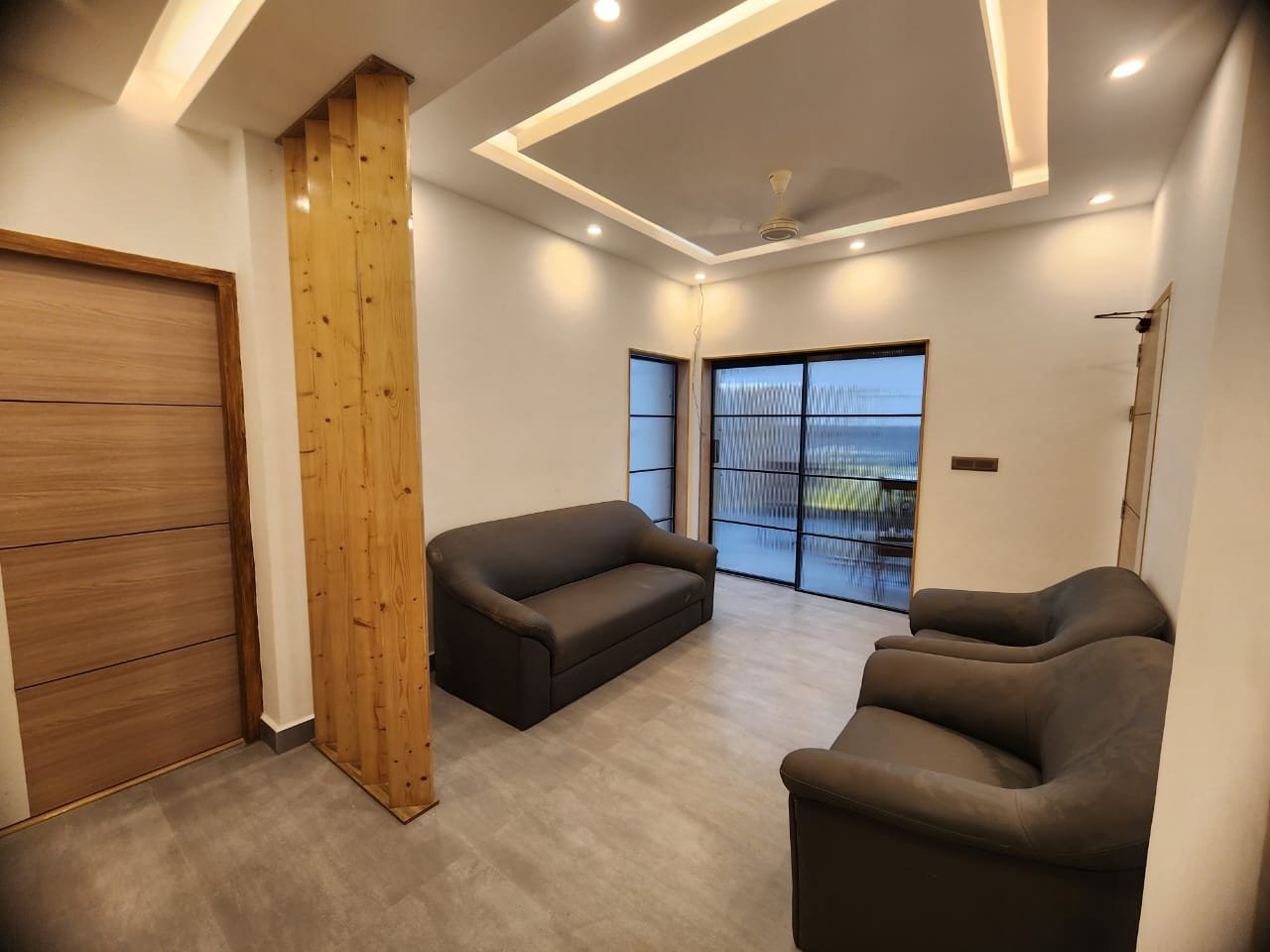 The waiting room at Align Dental Care: two dark brown armchairs, a timber-clad column, a cove-lit ceiling and black-framed glazing onto a balcony.