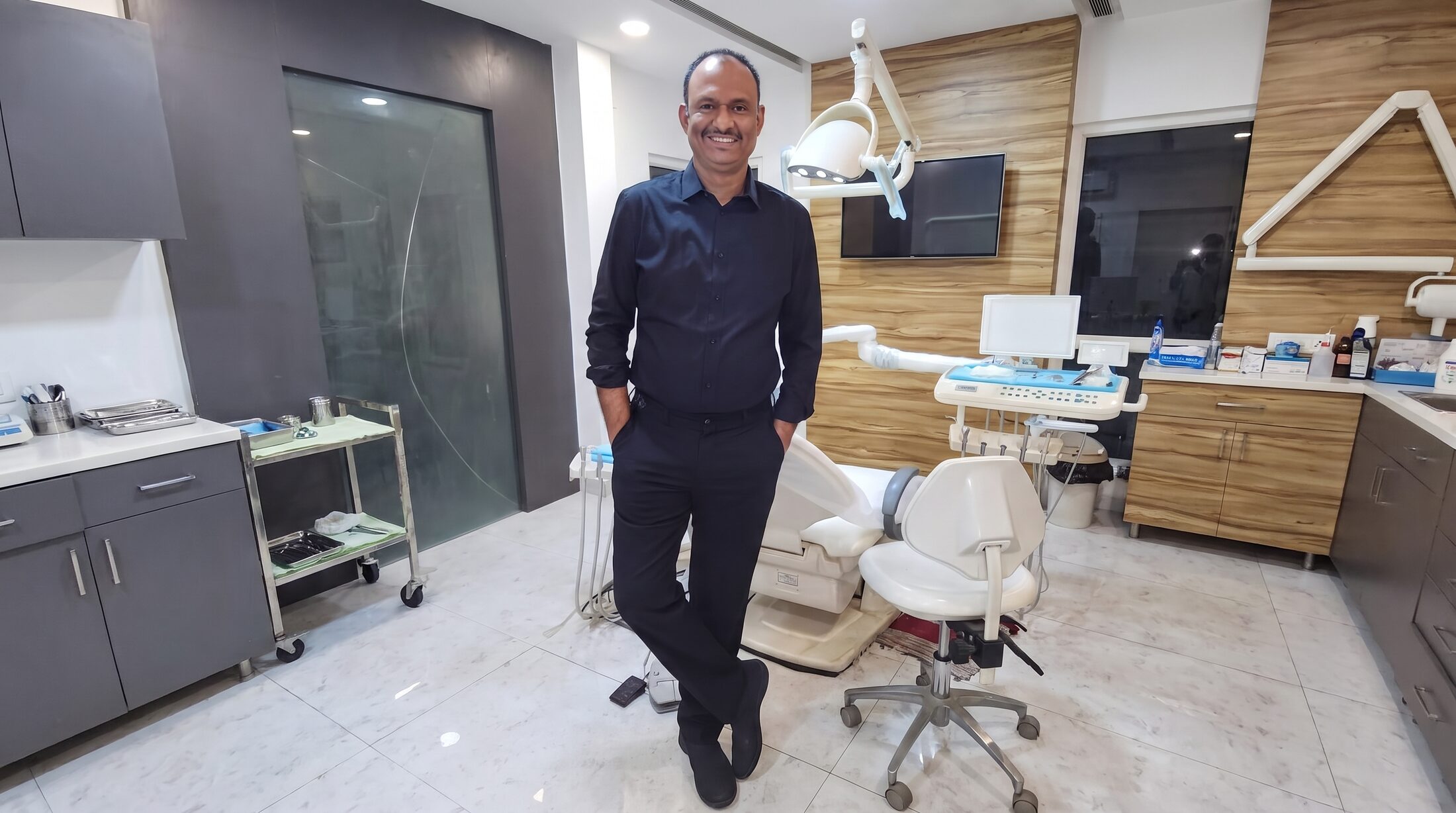 Prof. Dr S. Srinivas standing beside the chair in his operatory at Align Dental Care, the operating light and instrument tray beside him.