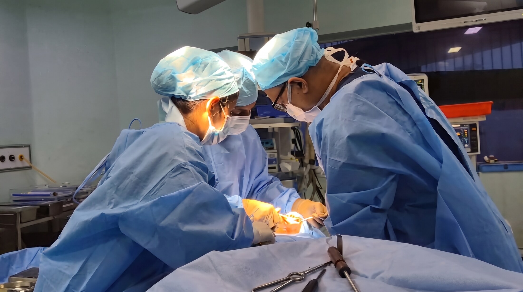 Two of the practice's surgeons operating together under the theatre light, gowned, masked and working over a draped patient.
