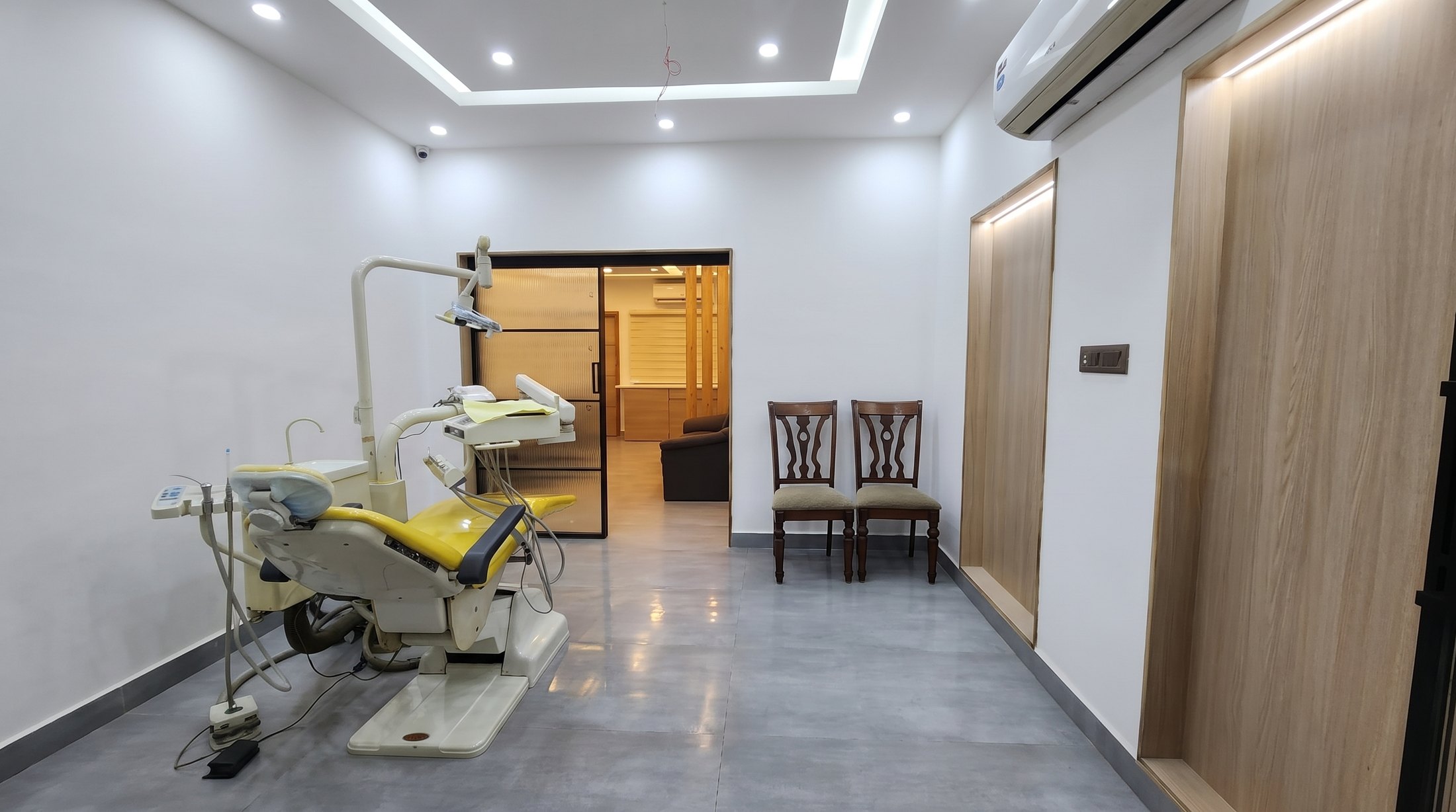 A treatment room at Align Dental Care looking down the surgery: the chair under its operating light on the left, the timber-panelled corridor and two waiting chairs beyond, and the room past the glazed sliding door.