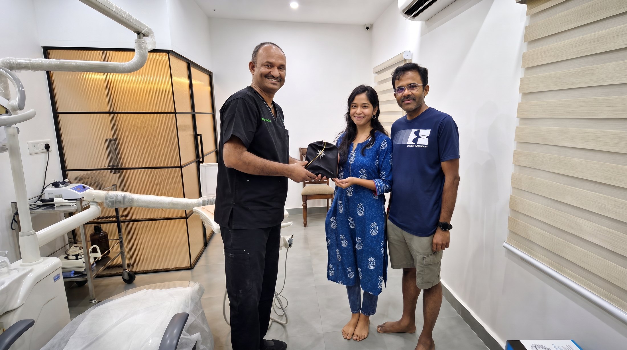 Prof. Dr S. Srinivas handing a patient her aligner case in a treatment room at Align Dental Care, with her companion beside her, all three smiling.